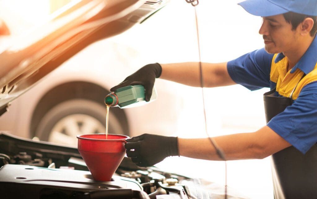 Mechanic wearing nitrile gloves adds oil to car engine.