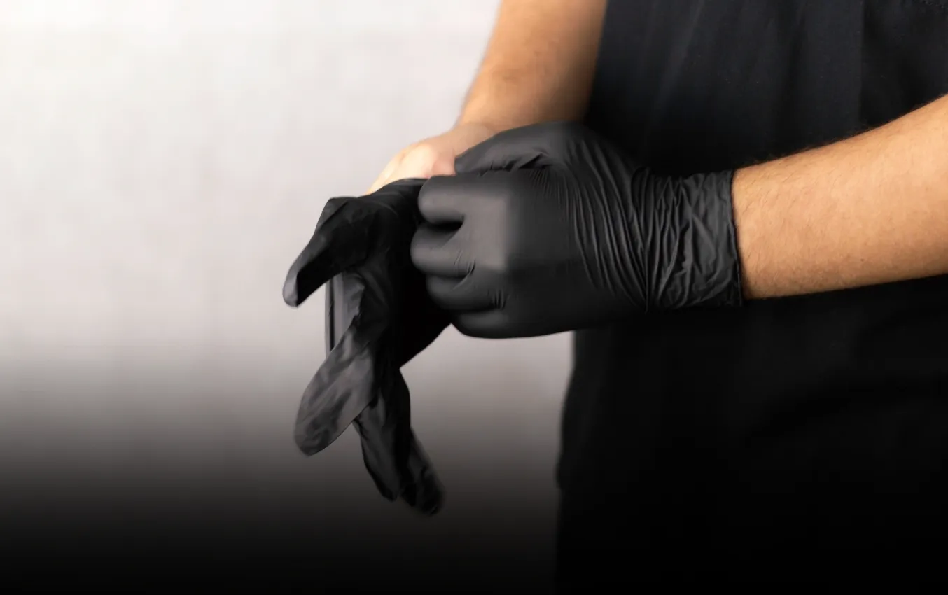 Person putting on black nitrile gloves, suitable for handling firearms and sensitive equipment.
