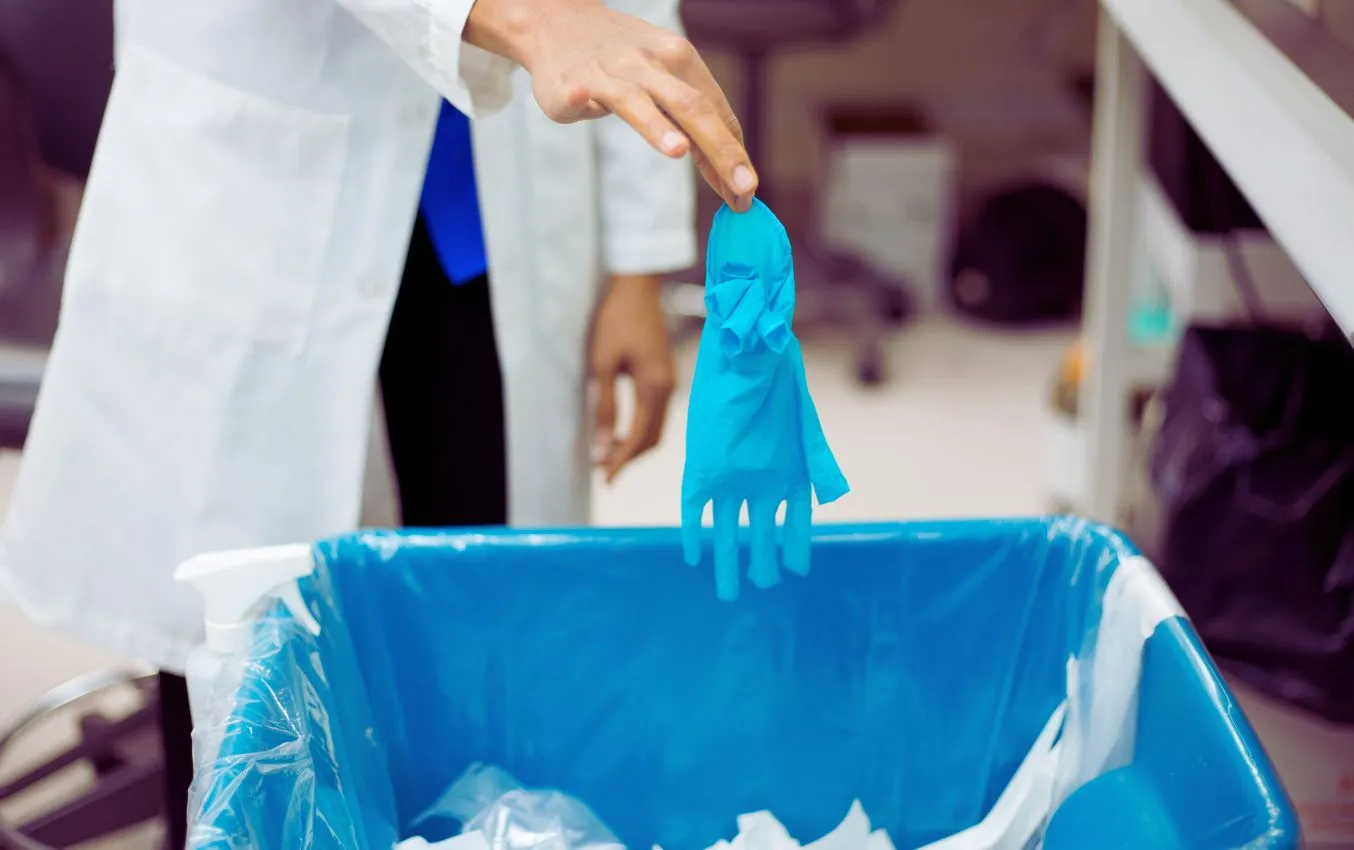 Person discarding used blue nitrile gloves into a recycling bin.